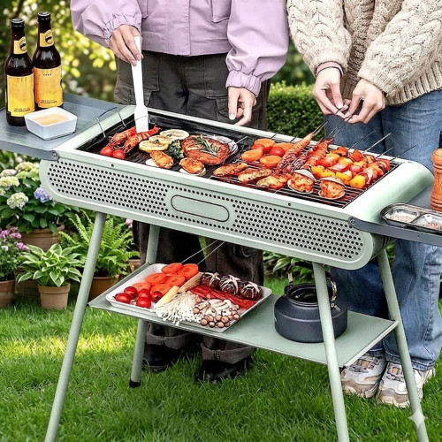 barbecue-charbon-portable-jardin-outdoor Barbecue à charbon blanc portable installé sur l'herbe avec des brochettes sur la grille et une étagère de rangement inférieure.