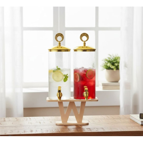 Double distributeur de boissons en verre avec robinets et couvercles dorés sur socle en bois contenant de la citronnade et du jus de fruits rouge.