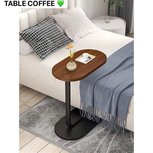 Table d appoint en forme de C avec plateau en bois foncé et pied métallique noir glissée contre un canapé blanc