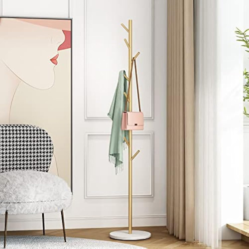 porte-manteau-sur-pied-design-arbre-dore Porte-manteau sur pied doré en forme d'arbre avec sac rose et écharpe verte sur un socle en marbre blanc.