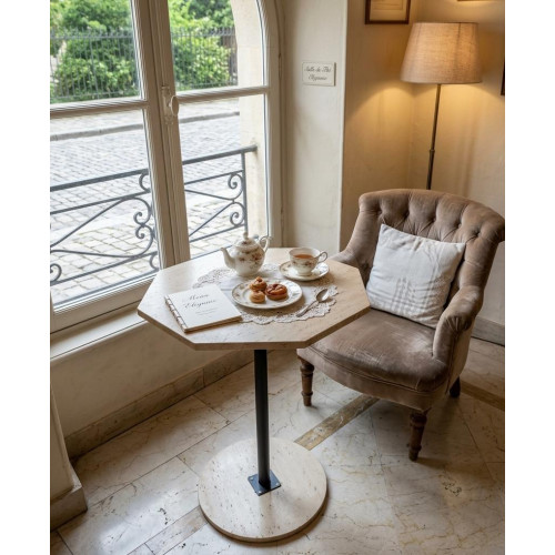 Table guéridon haute octogonale en travertin beige avec pied en métal noir et petits vases décoratifs posés sur le plateau.