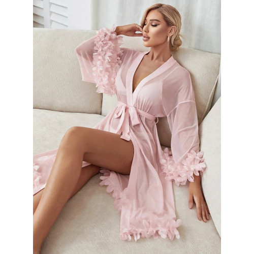 Femme aux cheveux blonds ondulés assise sur un canapé clair portant un kimono déshabillé long transparent rose clair avec des volants en plumes aux manches