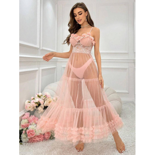 Femme assise sur un canapé blanc portant une longue robe nuisette transparente de couleur rose poudre avec bustier en dentelle