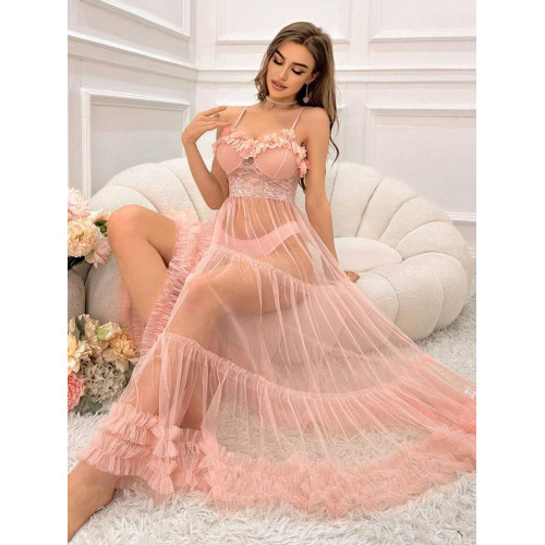 Femme assise sur un canapé blanc portant une longue robe nuisette transparente de couleur rose poudre avec bustier en dentelle