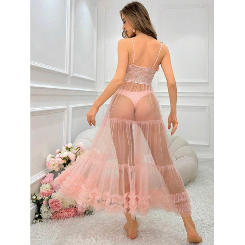 Femme assise sur un canapé blanc portant une longue robe nuisette transparente de couleur rose poudre avec bustier en dentelle