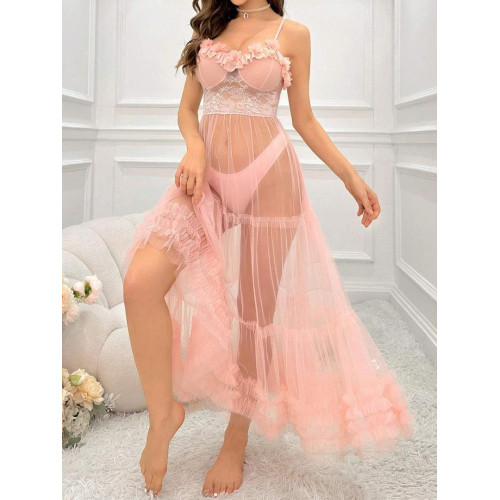 Femme assise sur un canapé blanc portant une longue robe nuisette transparente de couleur rose poudre avec bustier en dentelle